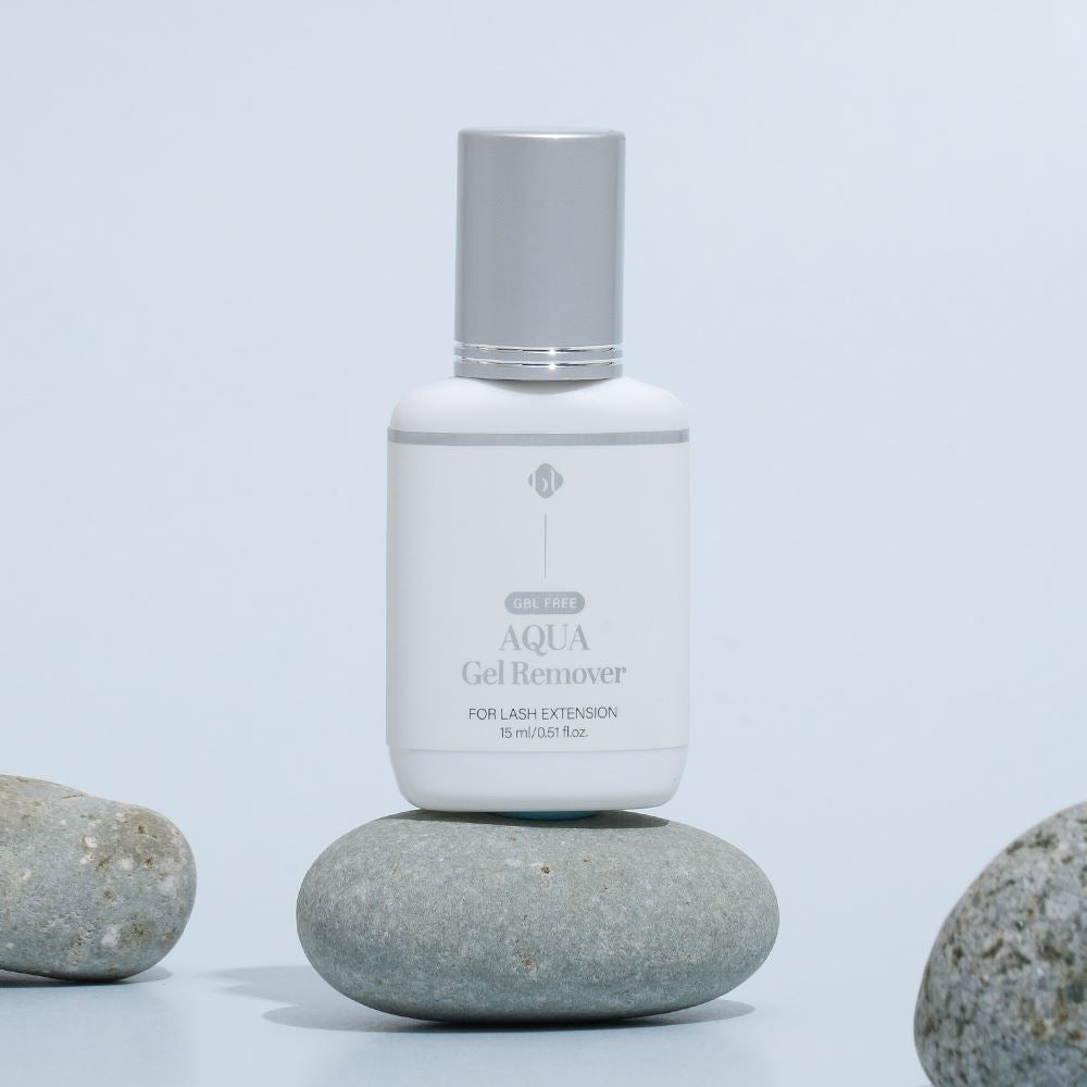 BL Lashes Aqua Gel Remover 15ml bottle with a silver cap resting on smooth grey stones against a light blue background.