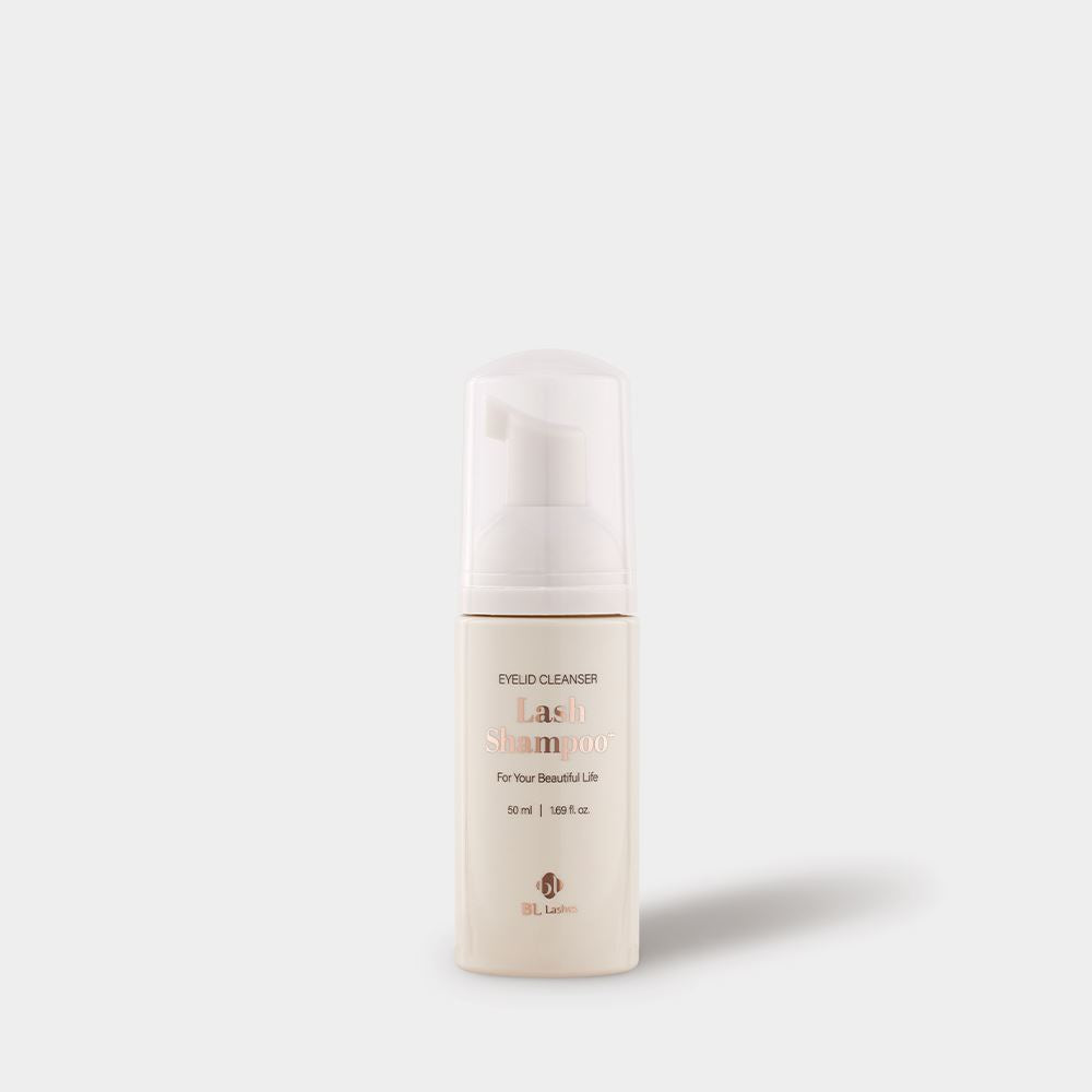 A beige BL Lashes Lash Shampoo eyelid cleanser bottle with a foaming pump and translucent protective cap is centered on a light gray background. The compact bottle with softly rounded edges features rose-gold and brown text reading “Eyelid Cleanser,” “Lash Shampoo,” “For Your Beautiful Life,” and “50 ml / 1.69 fl. oz.” A soft shadow falls to the lower right, highlighting the clean, minimal studio-style presentation of a professional lash cleansing product for eyelid hygiene and eyelash extension aftercare.