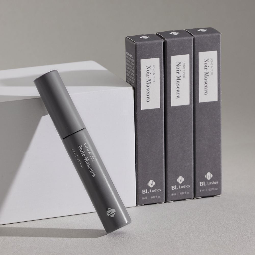"BL Lashes Noir Mascara tube leaning against a white block, displayed with three individual packaging boxes standing behind it.