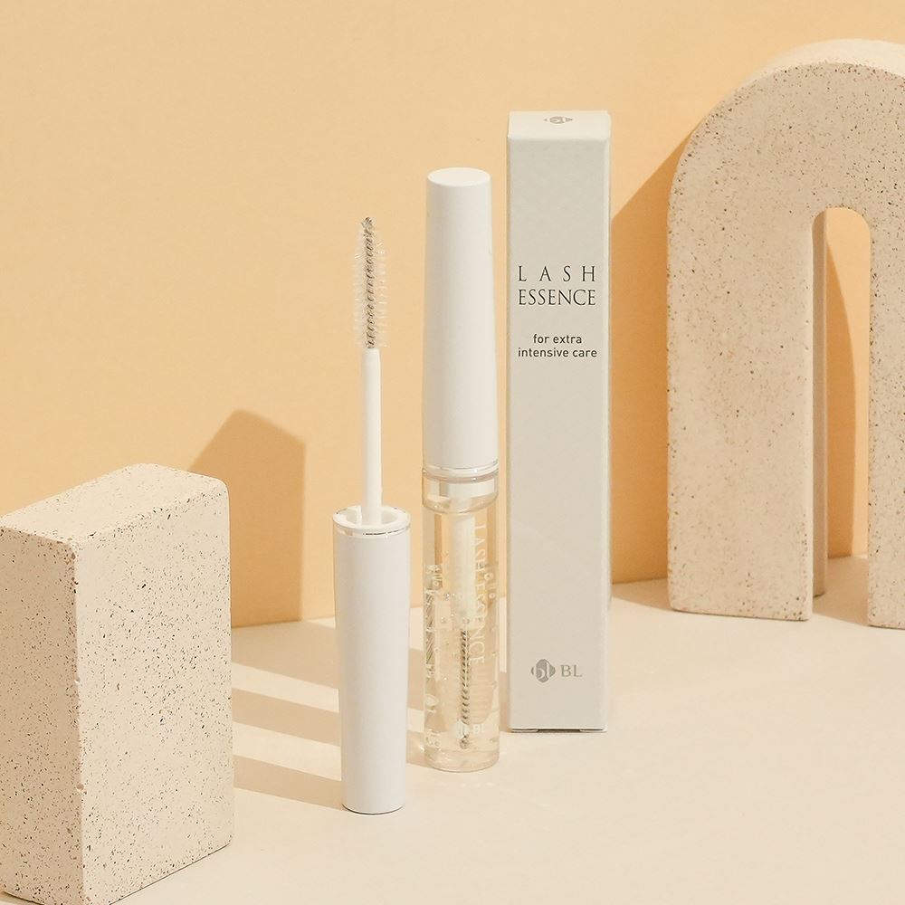 BL Lashes Lash Essence clear tube, opened wand applicator, and its white packaging box arranged with textured beige stone props.