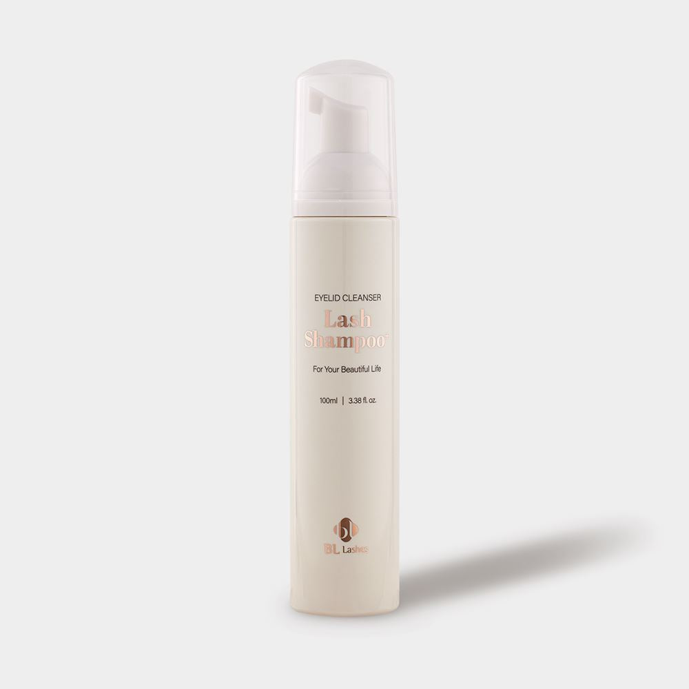 A minimal beige bottle of BL Lashes Lash Shampoo eyelid cleanser with a foaming pump dispenser and clear protective cap, placed on a light gray background with a soft shadow. The cylindrical bottle features rose-gold typography reading “Lash Shampoo” with smaller text “Eyelid Cleanser” and “For Your Beautiful Life,” along with the volume label “100 ml / 3.38 fl. oz.” The elegant cosmetic packaging highlights a clean, professional design used for eyelash extension aftercare and lash cleansing products.