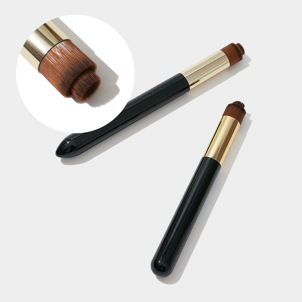 Two cosmetic cleansing brushes with soft brown bristles, gold metal ferrules, and glossy black handles are displayed on a light gray background. One brush lies horizontally while the other is angled diagonally, highlighting the compact rounded brush head. A circular inset zoom shows a close-up of the dense layered bristles designed for gentle eyelid and eyelash extension cleansing, emphasizing precision cleaning for lash shampoo use and professional lash care routines.