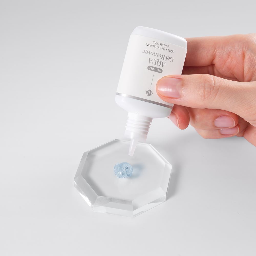 A hand dispensing BL Lashes Aqua Gel Remover for eyelash extensions onto a clear octagonal plate, demonstrating its clear gel texture.