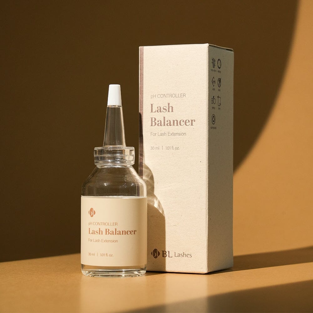 BL Lashes Lash Balancer pH Controller for lash extensions displayed in a clear glass bottle with a pointed applicator nozzle beside its beige product box on a warm-toned surface. The label reads ?œpH Controller Lash Balancer For Lash Extension??with the volume ??0 ml / 1.01 fl. oz.??Warm directional lighting casts soft shadows on the background, creating a professional beauty product composition that highlights lash preparation and pH balancing for eyelash extension treatments.